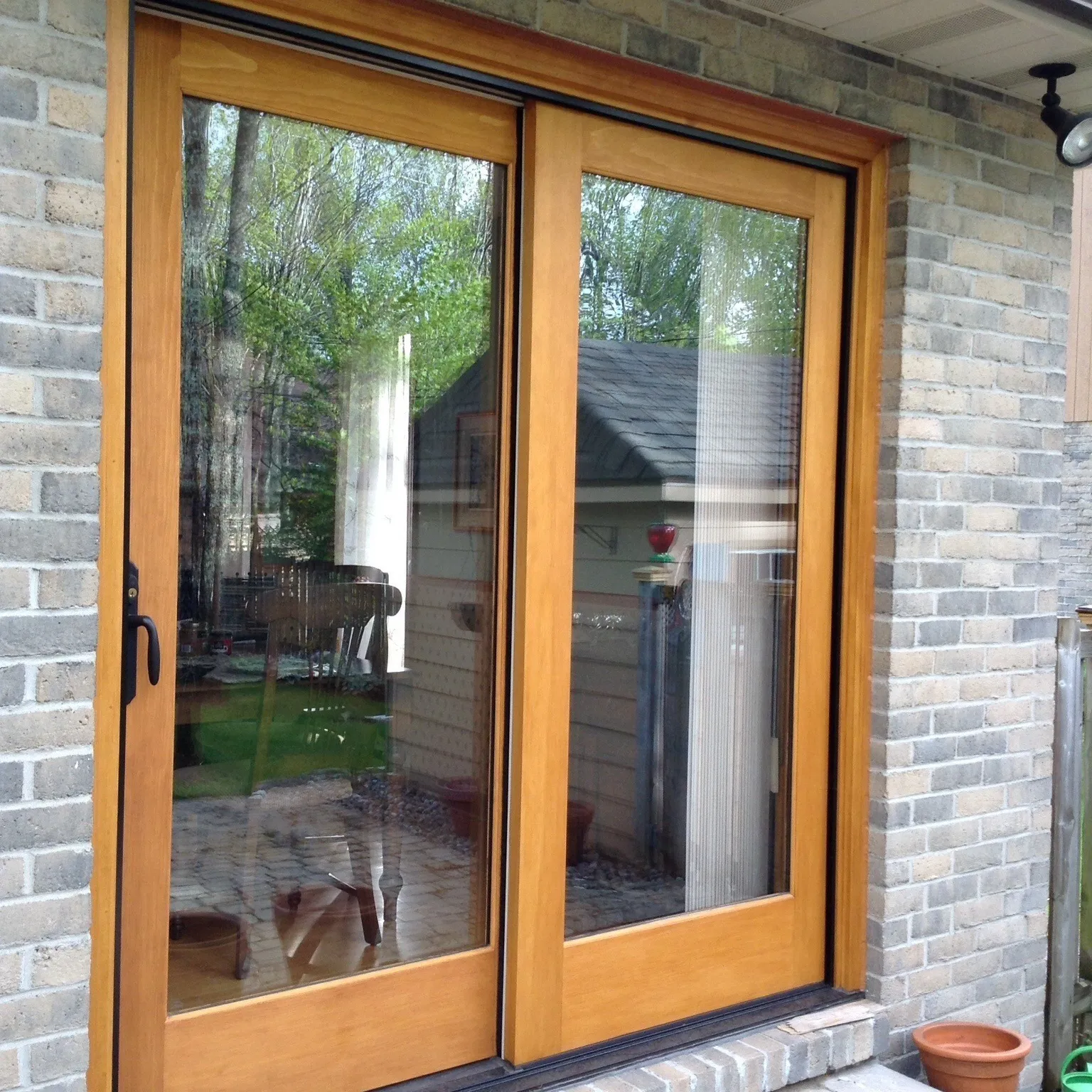 Exterior view of a wood sliding patio door set in grey brick, with a paver patio and clay pots.